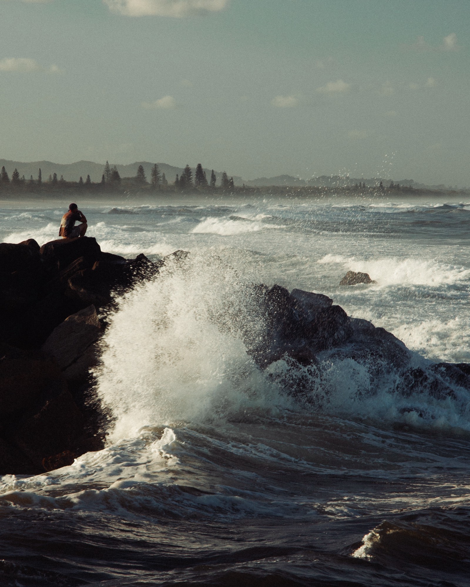 A figure sits in stillness as the Baltic sea breaks over the rocks